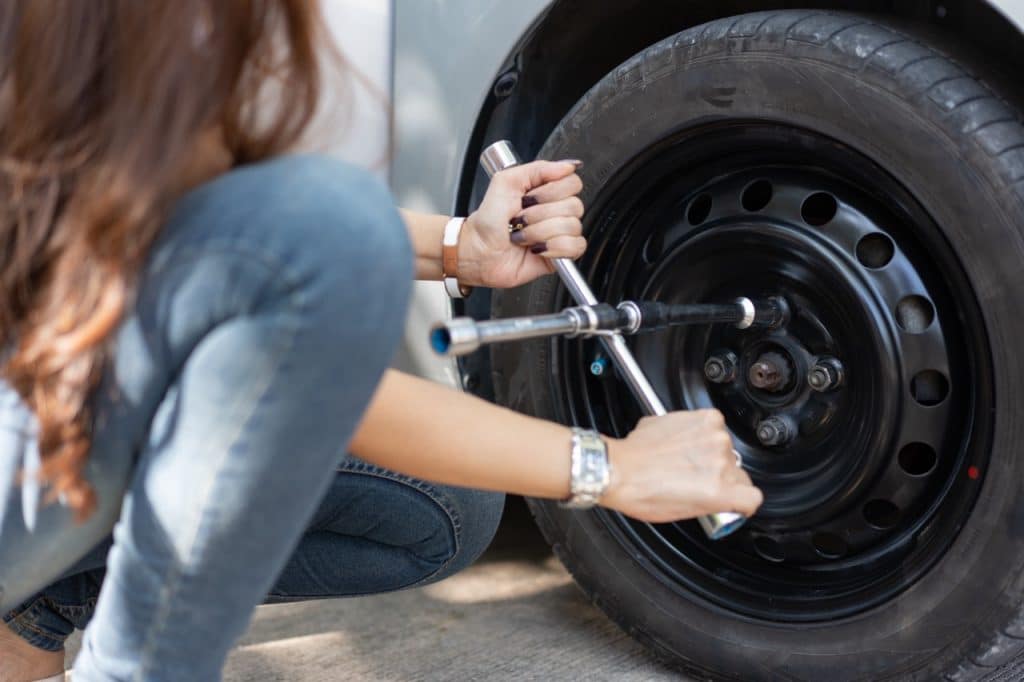 Une femme démonte la roue de sa voiture à l'aide d'un outil, une clé en croix pour desserrer les écrous.